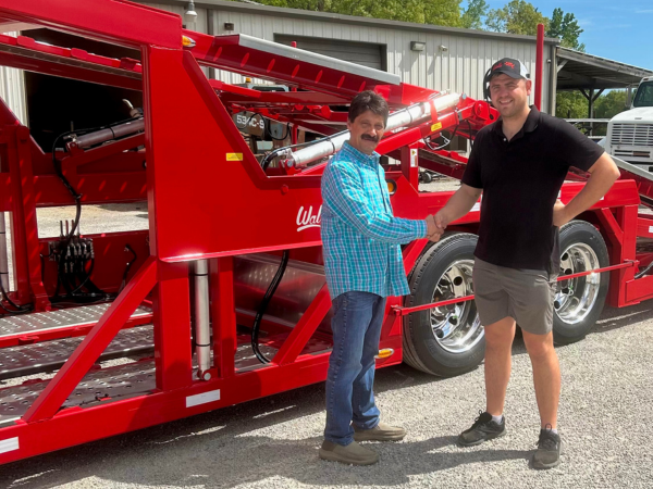 salesperson shaking hands with a customer standing in front of a red wally-mo car hauling trailer